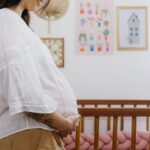 expectant mother standing beside a wooden crib in a beautifully decorated nursery room.