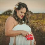 pregnant woman in countryside holding baby shoes, smiling and celebrating the joy of motherhood.