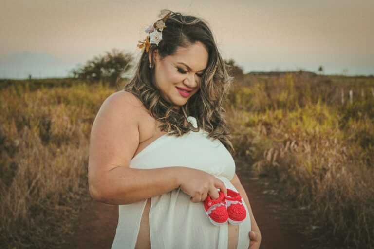 pregnant woman in countryside holding baby shoes, smiling and celebrating the joy of motherhood.