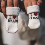 close-up of parents holding baby socks indicating pregnancy announcement, tagged with 'i love mum' and 'i love dad'.