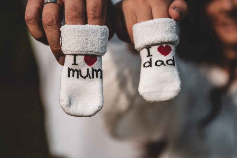 close-up of parents holding baby socks indicating pregnancy announcement, tagged with 'i love mum' and 'i love dad'.