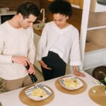 a pregnant couple preparing pasta in a cozy kitchen setting.