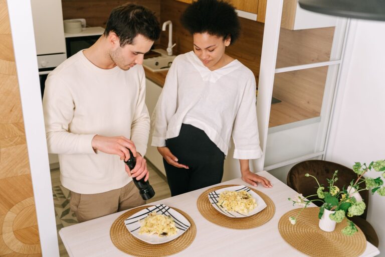 a pregnant couple preparing pasta in a cozy kitchen setting.