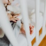 adorable baby sleeping peacefully in a crib, holding a soft toy next to a baby blanket.