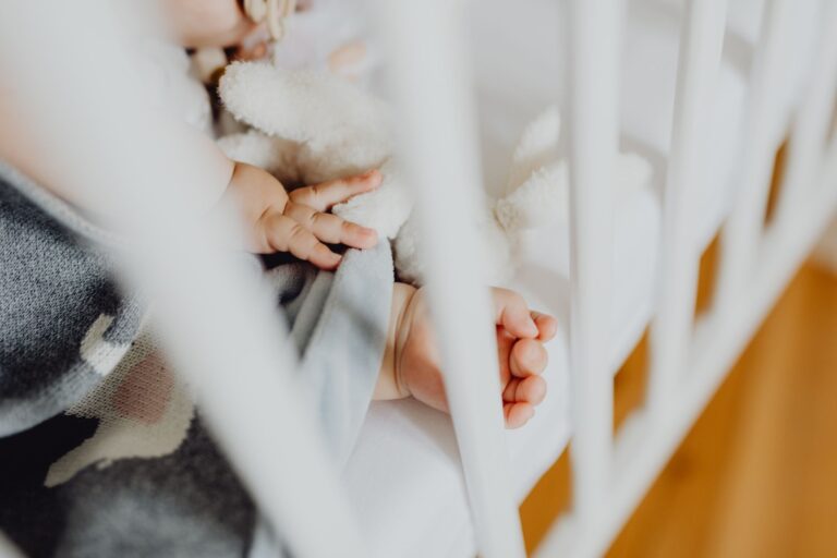 adorable baby sleeping peacefully in a crib, holding a soft toy next to a baby blanket.