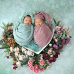 cute twin babies wrapped in pastel swaddles, nestled in a floral arrangement.