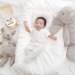 a cute one-month-old baby lying with plush toys on a bed, celebrating a special milestone.