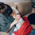 a tender moment of a mother comforting her sleeping baby while resting on a sofa indoors.