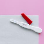 a positive pregnancy test with a red cap on a pink and white surface in a flat lay style.