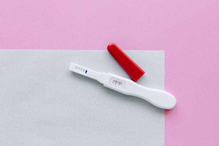a positive pregnancy test with a red cap on a pink and white surface in a flat lay style.