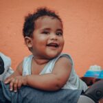 adorable baby sitting and smiling in a stroller with a vibrant orange background.
