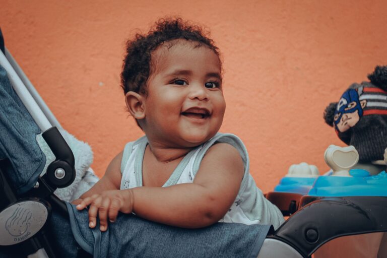 adorable baby sitting and smiling in a stroller with a vibrant orange background.
