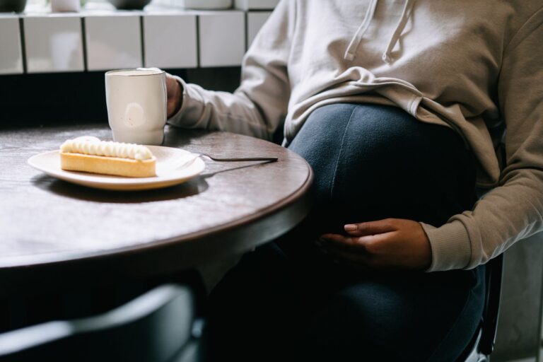 a close-up of a pregnant woman sipping coffee and enjoying a pastry indoors.