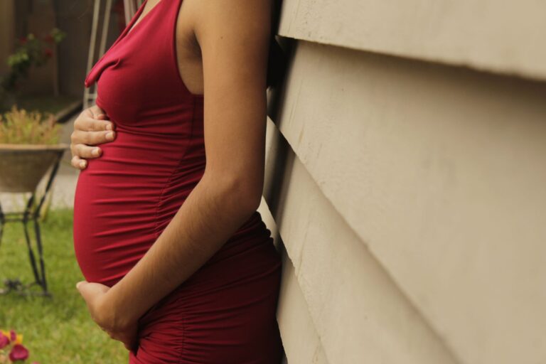 elegant maternity photo featuring a pregnant woman in a red dress outdoors.