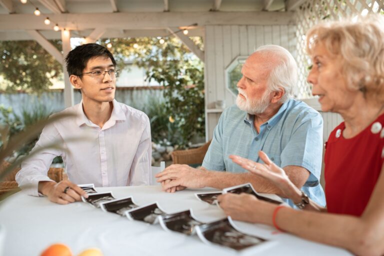 senior couple and family member discussing ultrasound photos at an outdoor table.