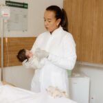 a medical practitioner gently holds a newborn beside a patient in a healthcare setting.