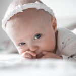 close-up of an adorable baby with a headband lying down and sucking thumb.