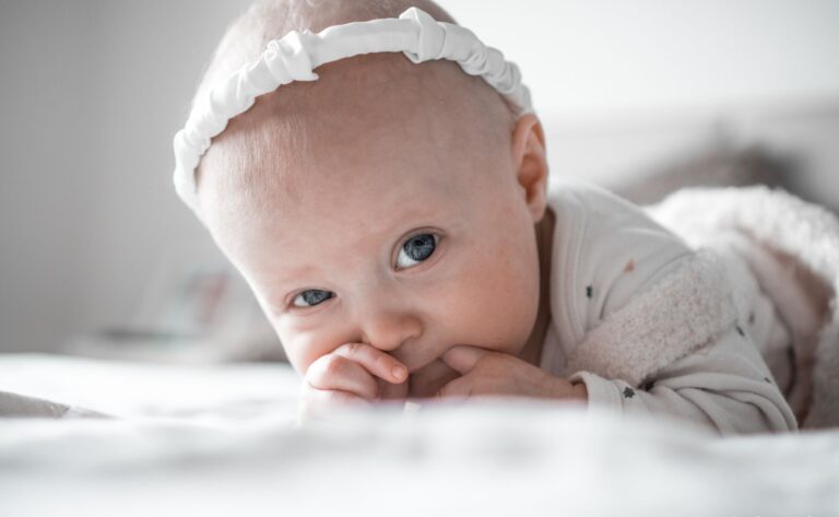 close-up of an adorable baby with a headband lying down and sucking thumb.