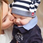 a mother lovingly kisses her smiling baby boy, creating a warm, affectionate scene.