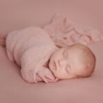 adorable newborn baby wrapped in a soft pink blanket, peacefully sleeping on a pastel background.