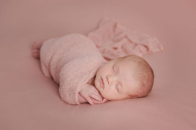 adorable newborn baby wrapped in a soft pink blanket, peacefully sleeping on a pastel background.